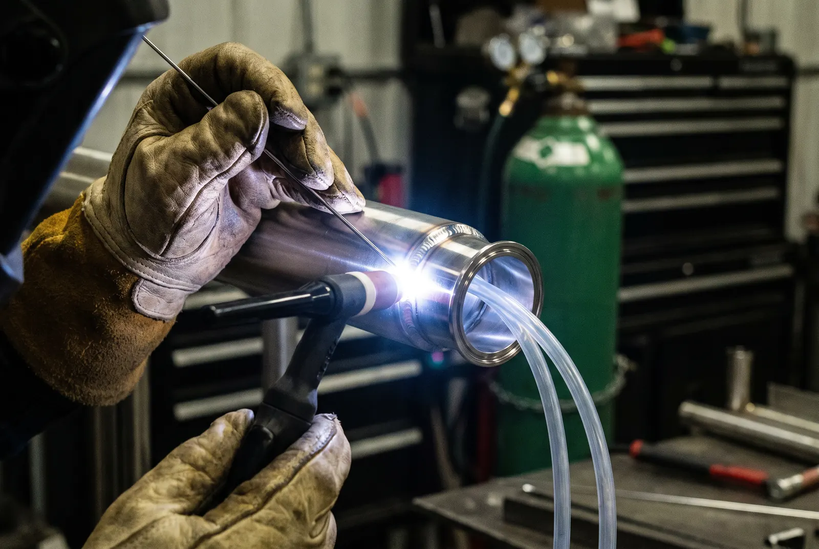 Soudage TIG d'un raccord de tube en acier inoxydable avec purge arrière, main gantée tenant la baguette d'apport, bouteille de gaz derrière